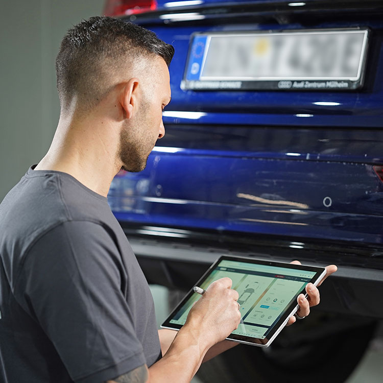 Kfz Gutachter in Duisburg erstellt digitalen Kostenvoranschlag mit Tablet vor einem blauen Audi