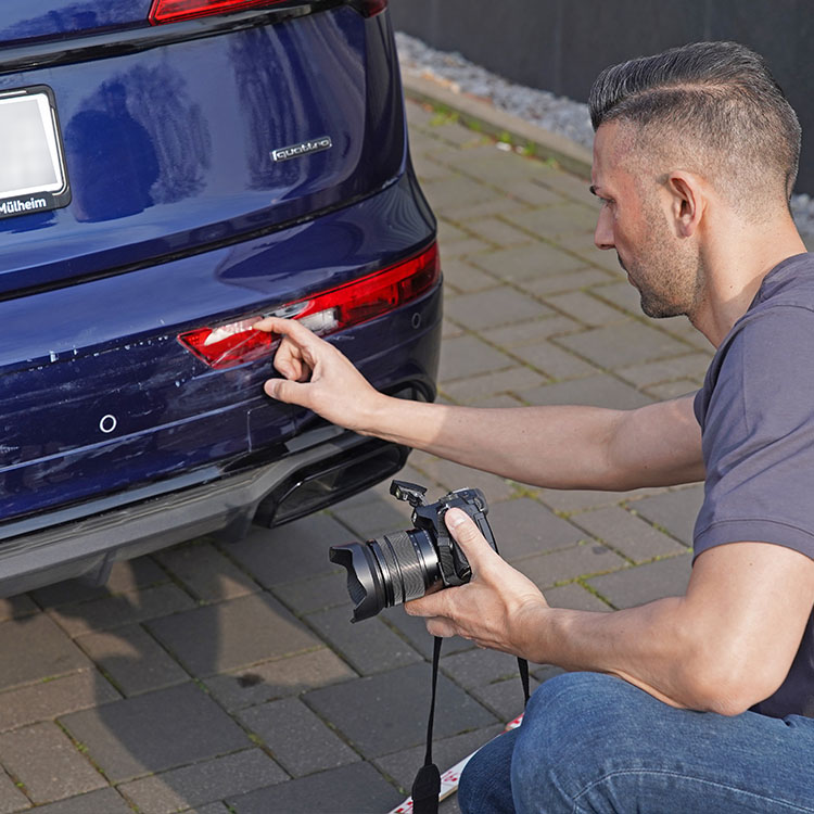Kfz Gutachter in Duisburg dokumentiert Heckschaden an einem blauen Audi mit Kamera